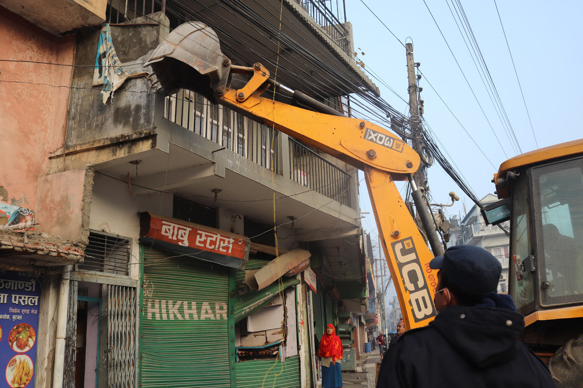 ट्राफिक चोकको एक घरमा डोजर चलाउँदैं गर्दा तलबाट हेरिरहेका एक सुरक्षाकर्मी र एक व्यवसायी !