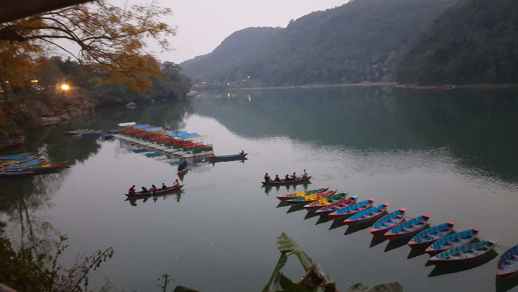 पोखरा महानगरपालिका वडा नं ६ गौरीघाटबाट देखिएको फेवाताल र ताल पारीबाट माछा मारेर फर्कदै गरेका स्थानीय । तस्वीर: जमुना वर्षा शर्मा, रासस